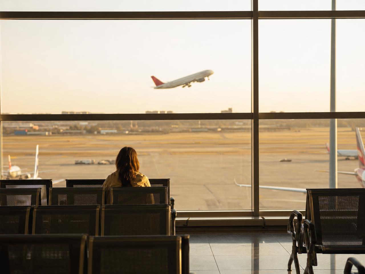 A person sitting alone in an airport terminal, watching a plane take off
